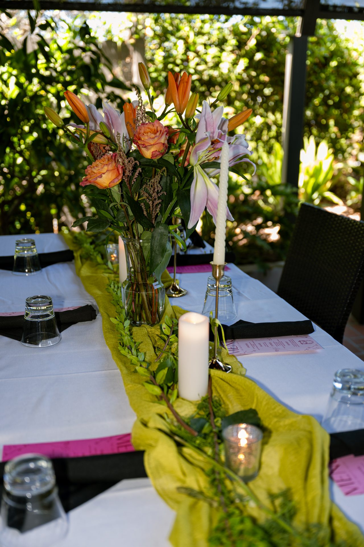 Orange lilies and pink roses rise above a candlelit table set against the garden’s greenery.