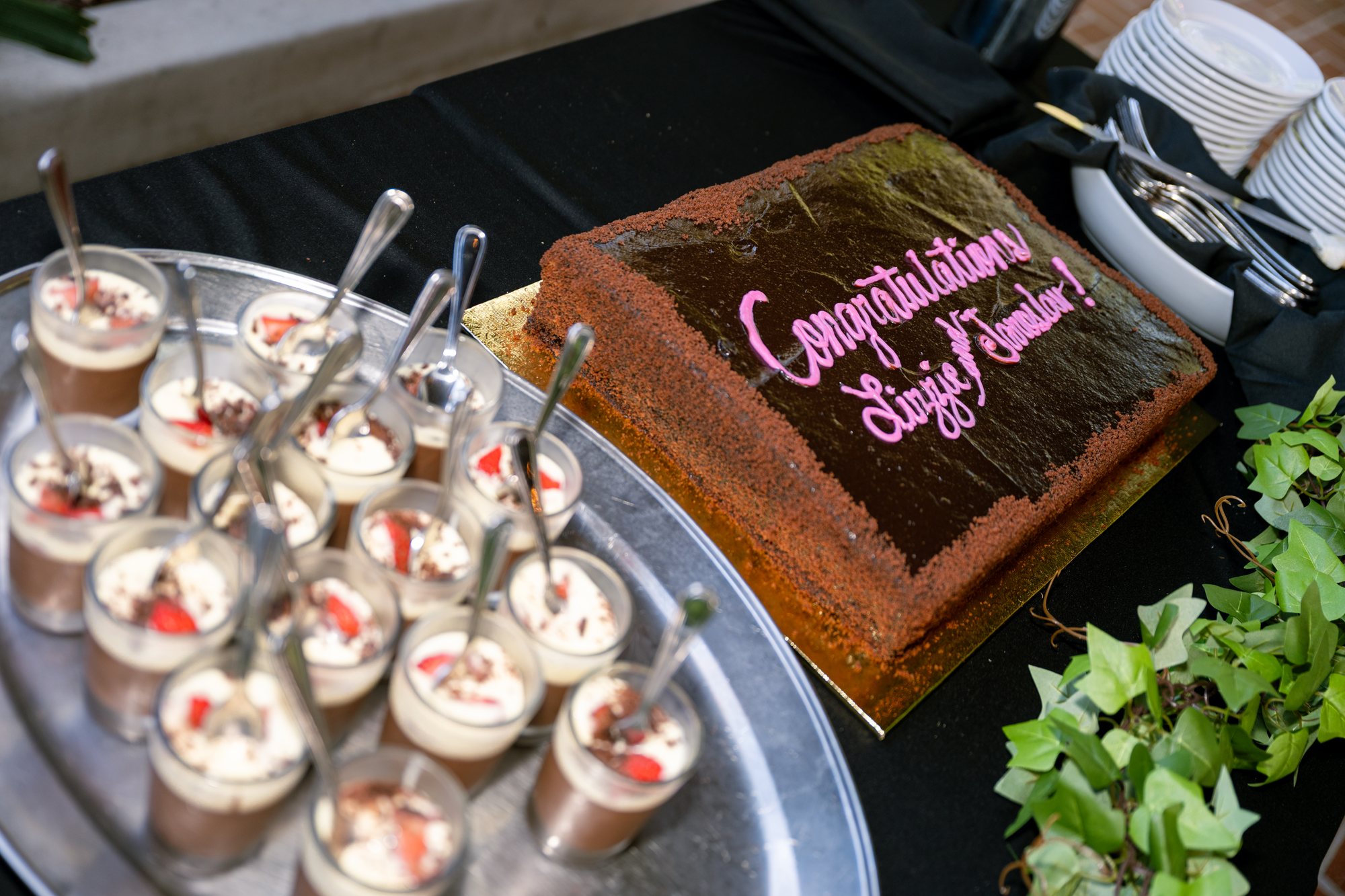 A chocolate engagement cake reading “Congratulations Lizzie and Jaroslav” sits beside individual desserts.